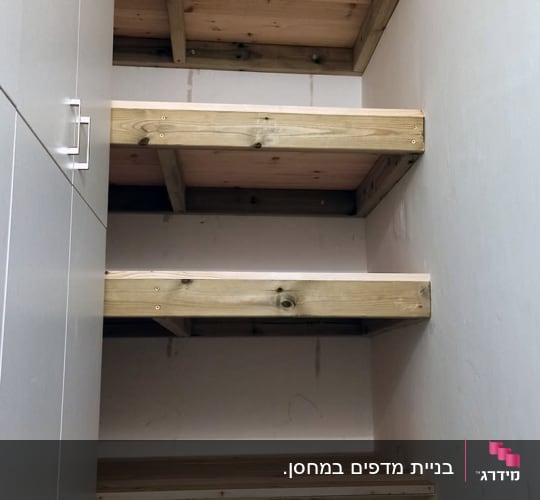 מדפי עץ מאסיביים מותקנים בתוך נישת אחסון לצד ארון לבן